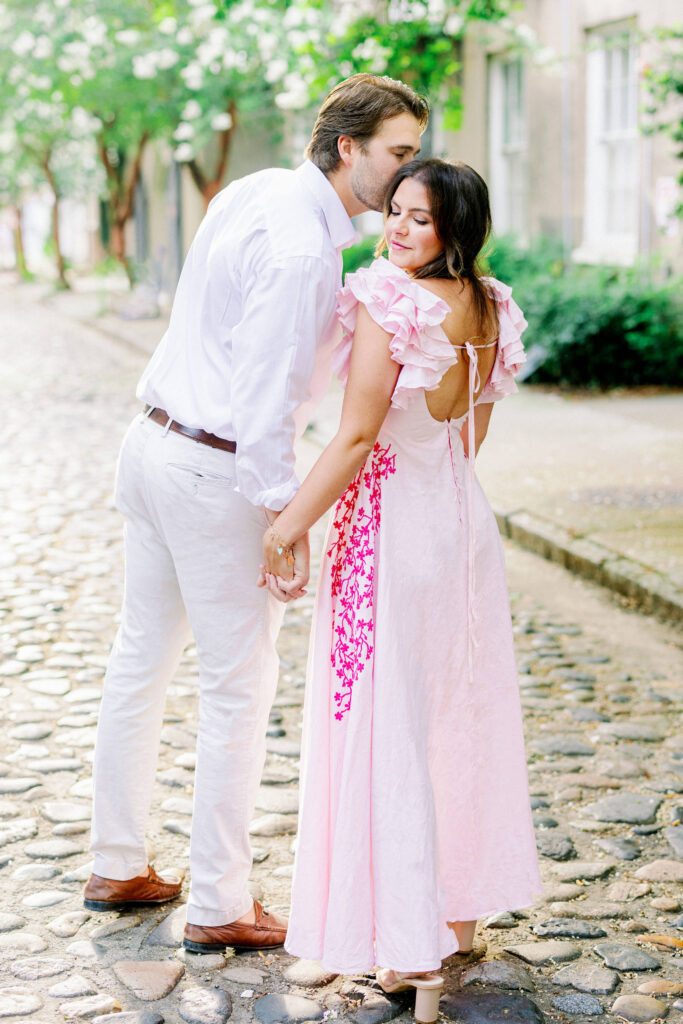 Man kissing woman in pink dress on cobblestone street in Charleston South Carolina